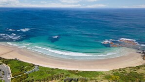 An aerial view of a beach with clear blue waters, a sandy shore, and some rocky outcrops.