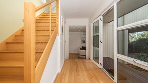 A modern interior with a wooden staircase, a hallway leading to a glass door, and a view of greenery outside. - Salty Shores Smiths Beach (Smiths Beach)