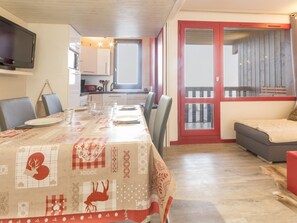 Uma área de refeições com uma mesa posta para quatro pessoas, uma cozinha ao fundo e uma varanda com guarda-corpo vermelho.