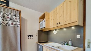 A compact kitchen with wooden cabinets, a microwave, a sink, and a refrigerator. - Cozy studio in village center, pets allowed, private parking (Samoëns)