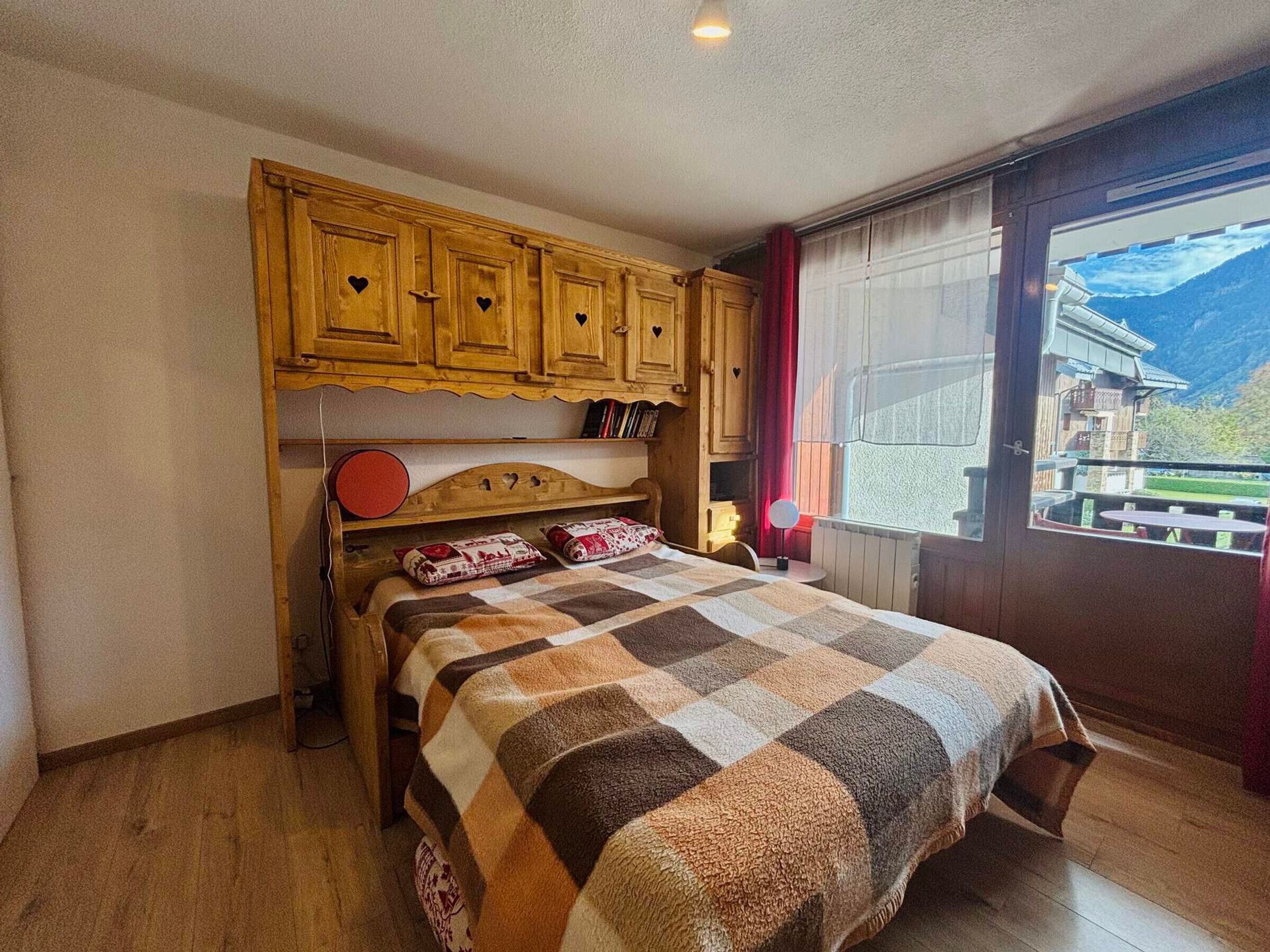 A bedroom with a wooden bed, a quilt, and a view of a mountain through a window.