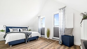 Ein Schlafzimmer mit einem großen Bett, einem Nachttisch, einer Topfpflanze und Blick auf den Himmel durch ein Fenster.