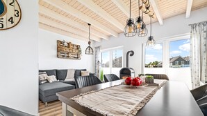 Ein modernes Wohnzimmer mit Holzbalkendecke, einem großen Fenster, einer Couch, einem Esstisch und einer Wanduhr als Dekoration.