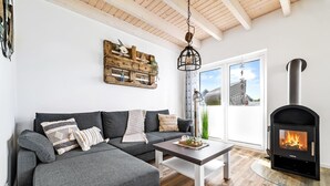 Ein modernes Wohnzimmer mit einem grauen Ecksofa, einem Holztisch und einem schwarzen Kaminofen.