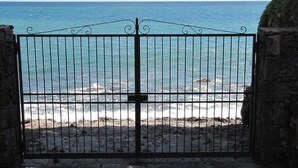 Een metalen poort die uitkomt op een strand, met golven die op de kust breken.