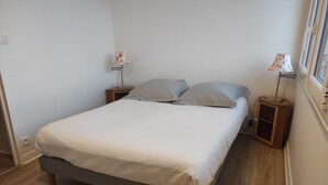 Ein ordentlich bezogenes Bett mit grauem Gestell und weißer Bettwäsche, zwei Nachttische mit Lampen sowie Holzboden.