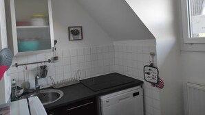Eine Küche mit weißen Fliesen, einer schwarzen Arbeitsplatte, einem Spülbecken, einem Geschirrgestell, einem Besen und einer kleinen Kakteendekoration.