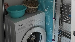 Ein kleiner Waschraum mit Waschmaschine, Wäscheständer, Spiegel und Ablage für Reinigungsmittel.
