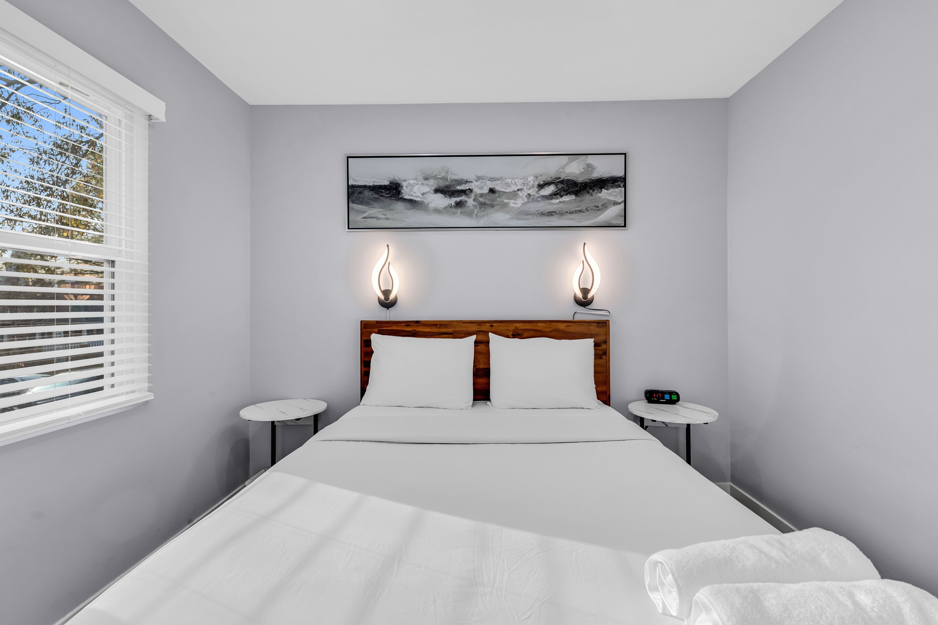 A modern bedroom with a large bed, two bedside tables, a nightstand, and a wall-mounted artwork.