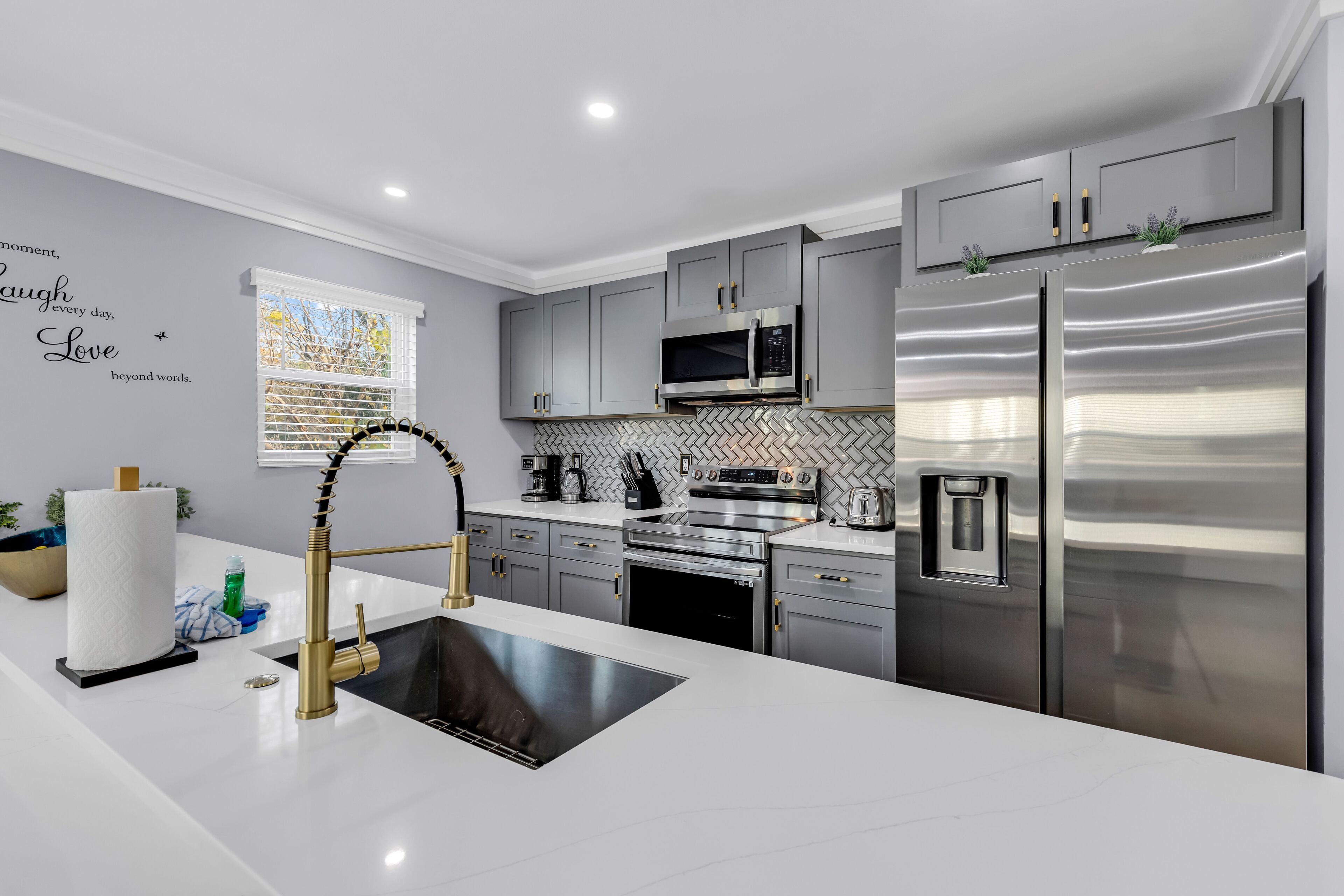 A modern kitchen with grey cabinets, stainless steel appliances, and a white countertop.