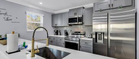 A modern kitchen with grey cabinets, stainless steel appliances, and a white countertop.