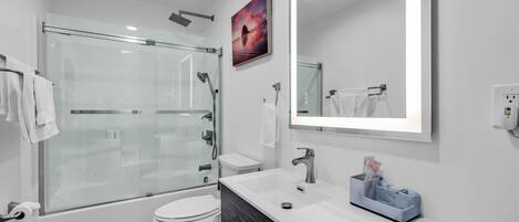 Un baño moderno con ducha envuelta en vidrio, inodoro blanco y tocador con espejo.