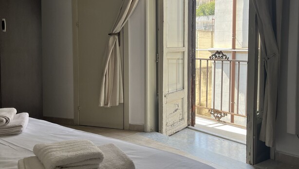 A bedroom with a bed, two towels, a door, and an open balcony door.