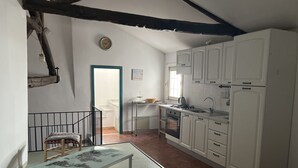 A compact kitchen with white cabinets, a small dining table, and a staircase leading to an upper level.