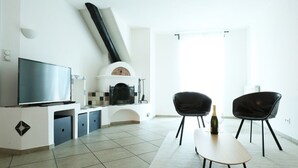 A modern living room with a flat-screen TV, a fireplace, two black chairs, and a table with a bottle and glass. - "Lichtenegg" apartment with garage in Merano (Merano)