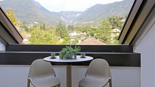A balcony with a table and two chairs, overlooking a mountainous landscape with houses. - "Lichtenegg" apartment with garage in Merano (Merano)