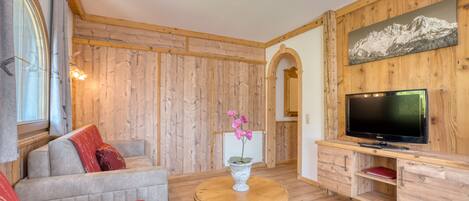Un salon chaleureux avec un mur en bois, un canapé, un téléviseur et une petite table sur laquelle est posé un vase de fleurs.