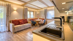 Une cuisine moderne dotée d’un évier encastré, de poutres en bois, d’un coin repas avec une table et des chaises, et d’un canapé agrémenté de coussins rouges.