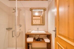A bathroom with a glass-enclosed shower, a wooden vanity with a sink, and a mirror above it. - Appartement Hofmann (Wald im Pinzgau)