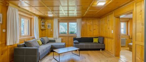 L’intérieur d’un chalet en bois comprend deux canapés, une table basse et de grandes fenêtres offrant une vue sur les montagnes.