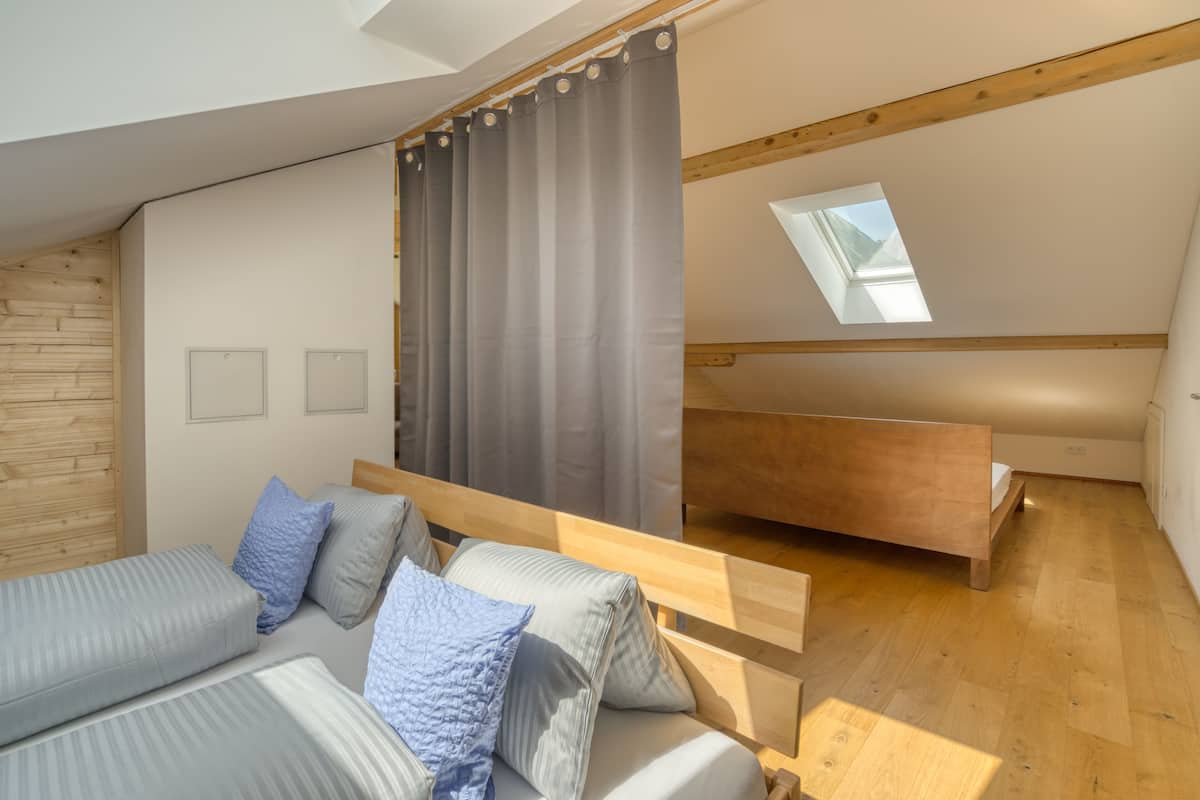A modern loft bedroom with a sloped ceiling, wooden beams, a skylight, and a built-in bench.