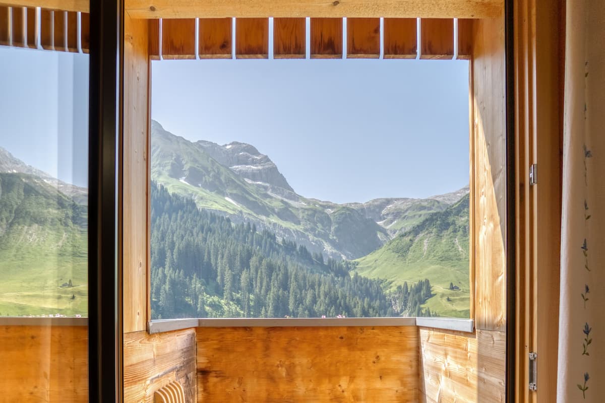 A wooden cabin with a bench and a large window offering a mountain view.