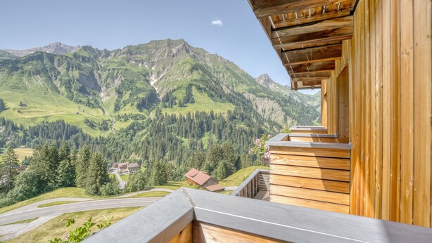 A wooden balcony with a view of a mountainous landscape, including a road and buildings. - HUS 24 (Schroecken)