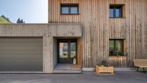 A modern building with a garage, a wooden facade, and a bench outside. - HUS 24 (Schroecken)