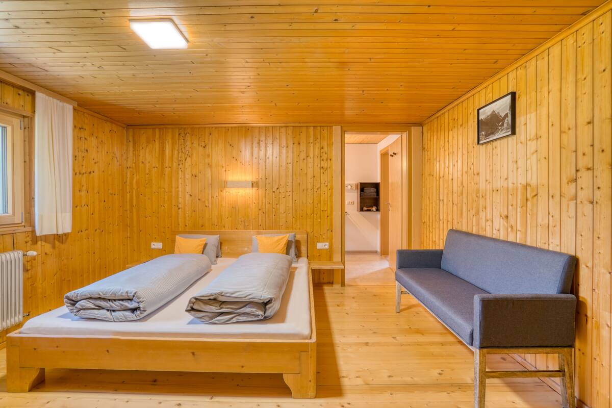A wooden-paneled room with a bed, a bench, and a picture on the wall.