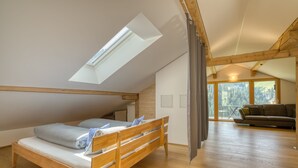 A loft bedroom with a skylight, wooden floor, a bed, a sofa, and a view of trees through large windows. - HUS 24 (Schroecken)