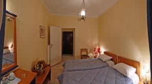 A hotel room with two beds, a wooden bench, a small table with a vase of flowers, a mirror, and a door leading to another room. - Hotel Marily (Pyrgos)
