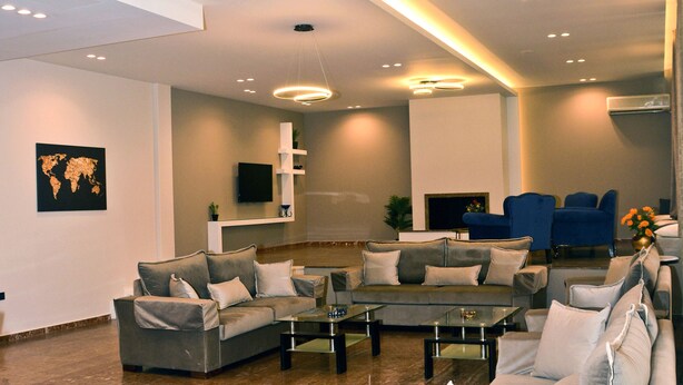 A modern living room with a sectional sofa, a glass coffee table, and a flat-screen TV mounted on the wall. - Hotel Marily (Pyrgos)
