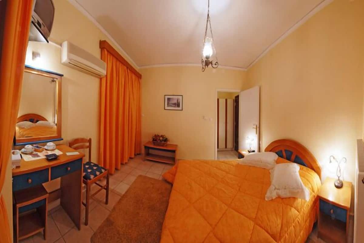 A bedroom with a bed, a desk, a chair, a bedside table, and a mirror.