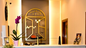 A hotel reception desk with a marble counter, a potted plant, and a decorative sign above the desk. - Hotel Marily (Pyrgos)