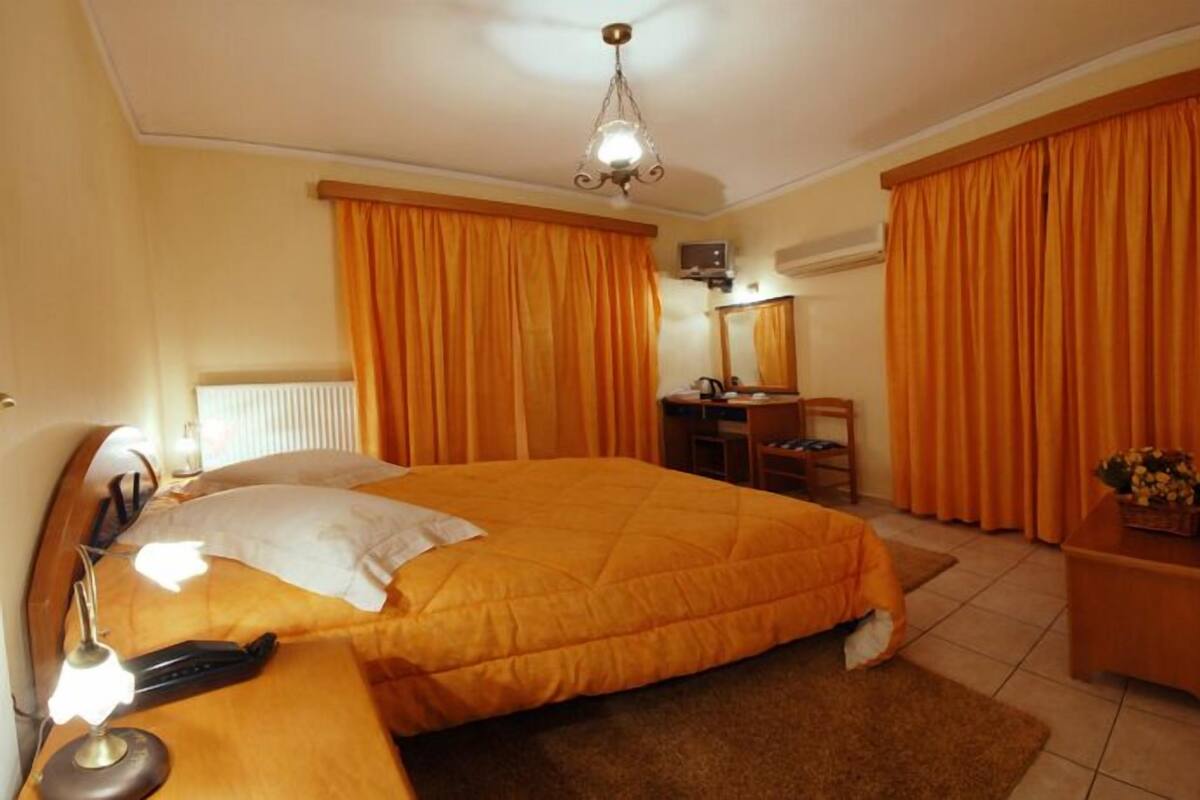 A hotel room with a large bed, a desk, a chair, a desk lamp, and a mirror.