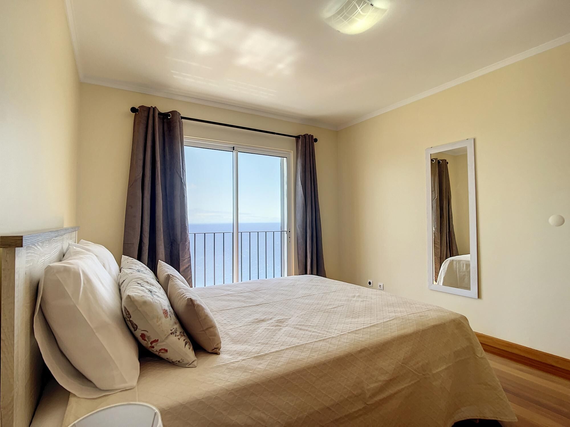 A bedroom with a bed, curtains, a window with a view, and a mirror.