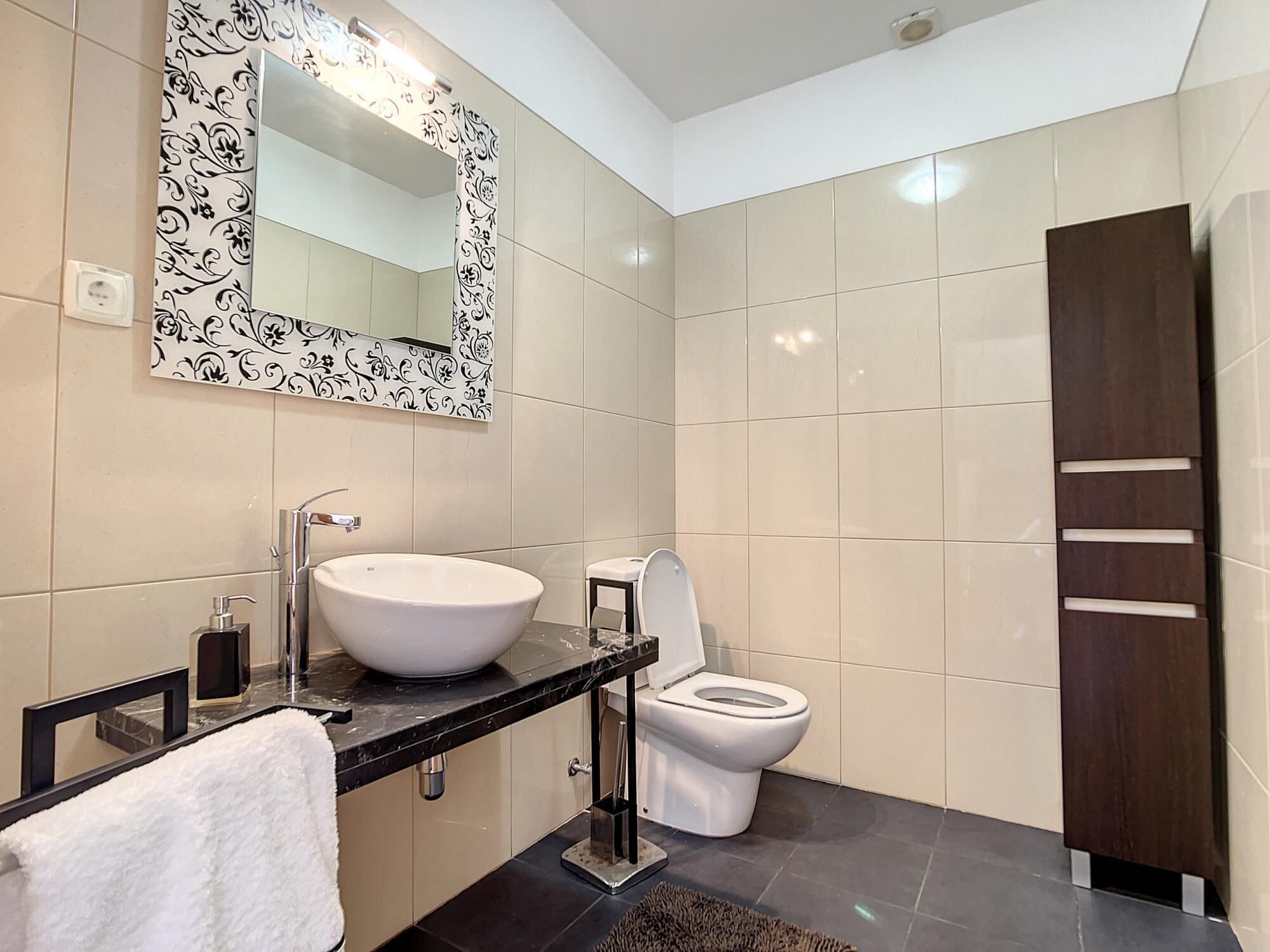 A modern bathroom with a large white sink, a toilet, and a mirror with a decorative frame.