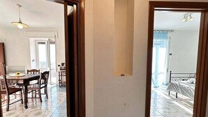 A room with a bed, a desk, and a chair. There is a door leading to another room.
