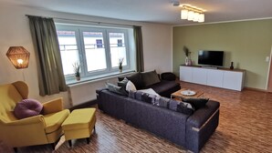 A living room with a sofa, armchair, and a TV on a cabinet. - Apartment "Blütezeit"- Ferienhof Gräfe restored 3-sided farm with pool & sauna (Meißen)