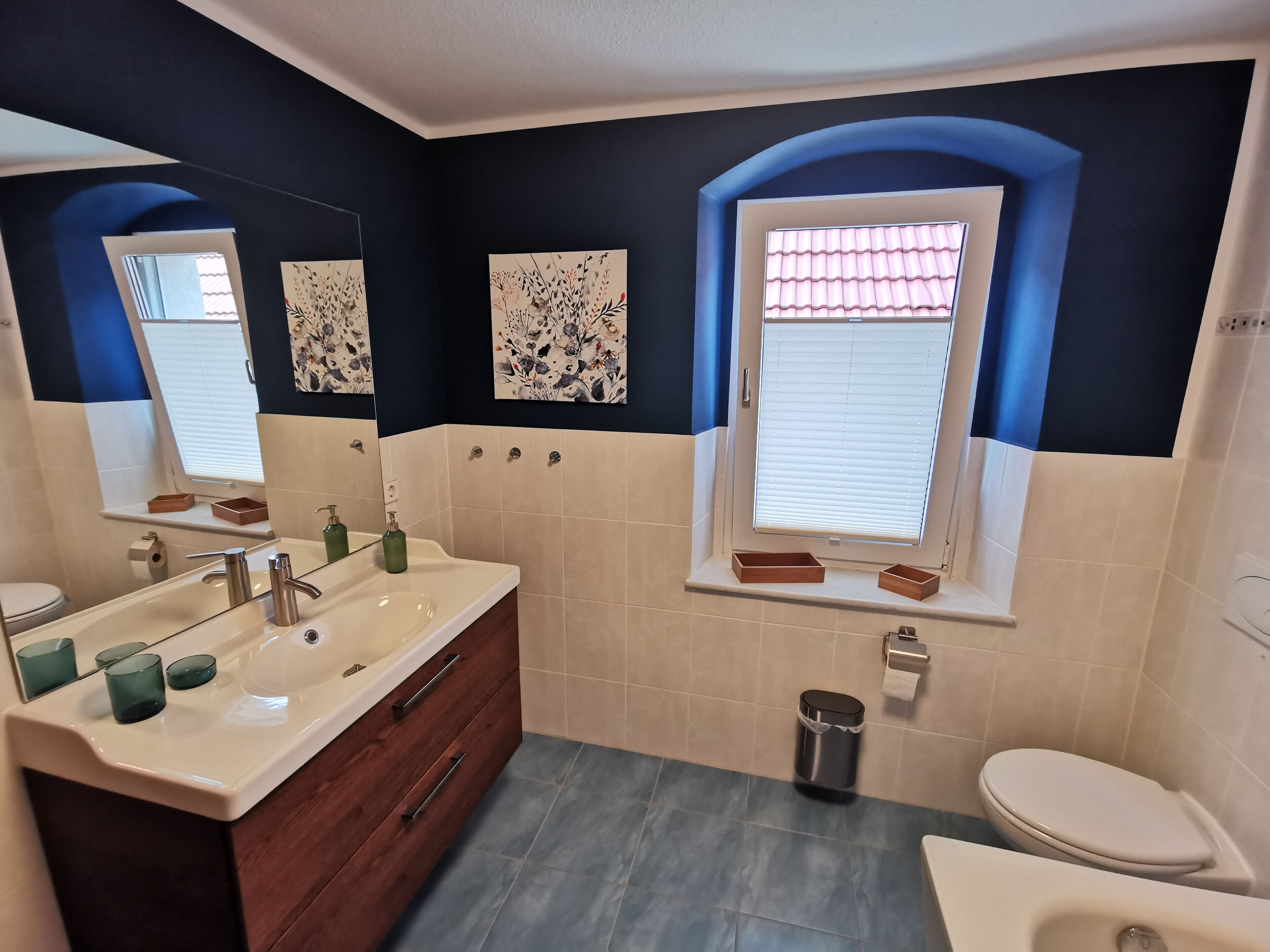 Ein modernes Badezimmer mit einem großen Waschtisch, einer Toilette und einem Fenster mit Jalousien.