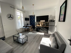 Een moderne woonkamer met een bank, een salontafel en een televisie. Er is een keuken met een koelkast, magnetron en fornuis.