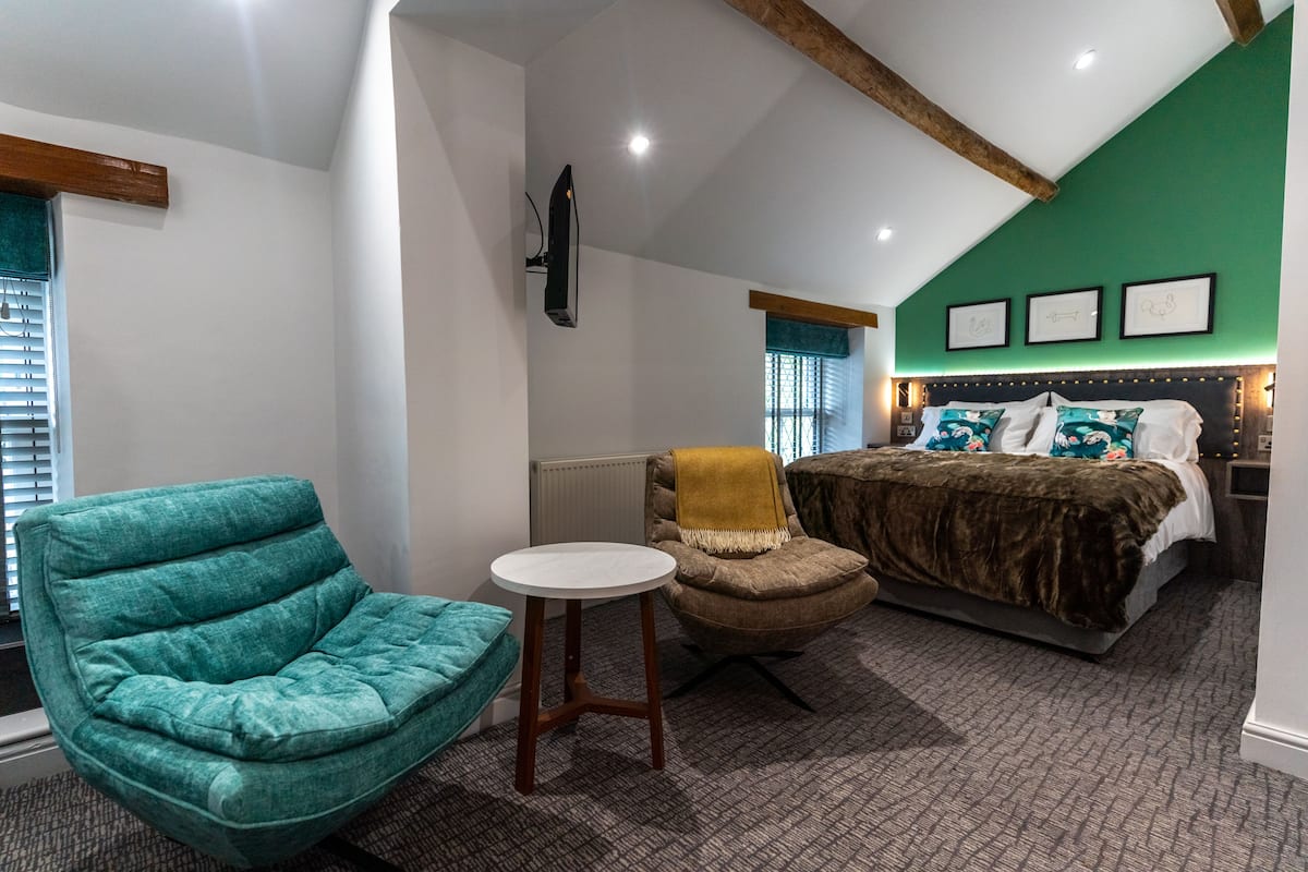 A bedroom with a bed, a green wall, a wooden ceiling beam, and a green armchair.