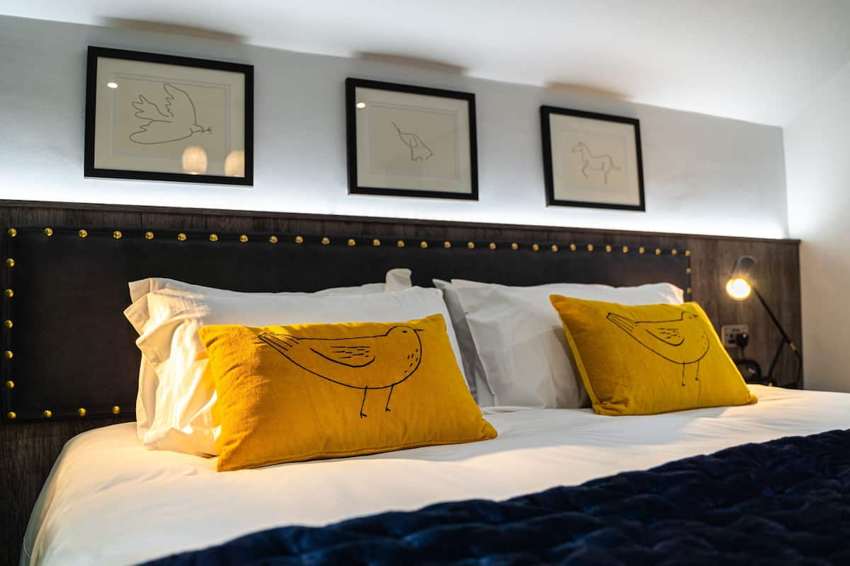 A bed with white and yellow pillows, a dark headboard, and framed artwork on the wall.
