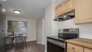 A modern kitchen with a built-in oven, a stainless steel range, wooden cabinets, and a dining area with a table and chairs. - A Home A Way from your Home with 3-bedroom & 2 bathroom with free parking  (Portland)