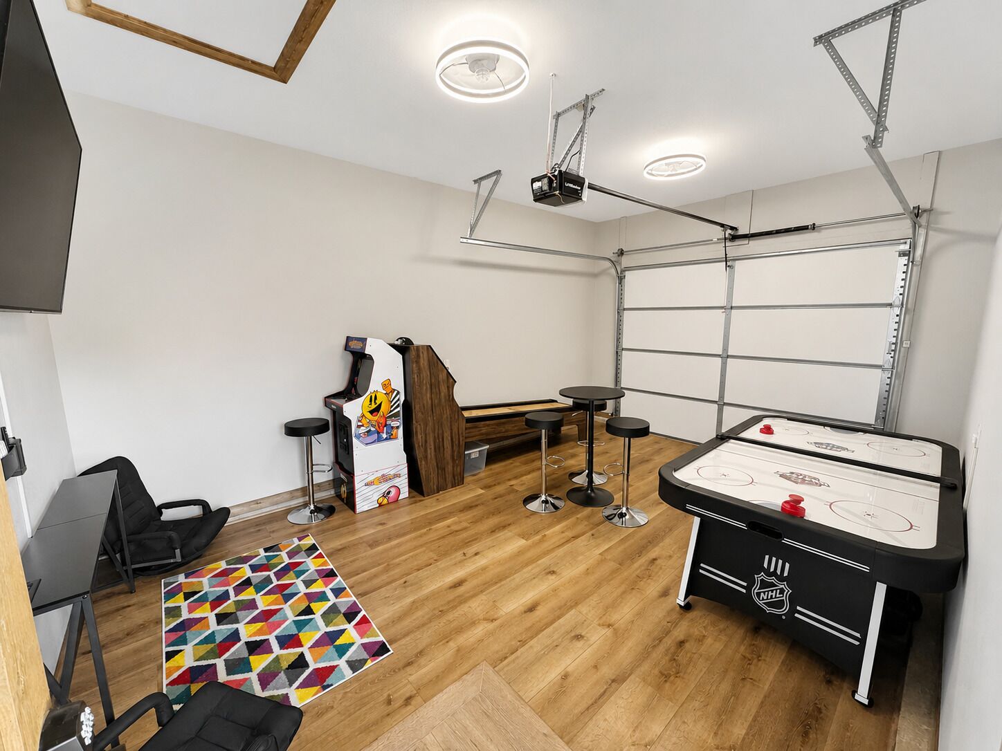 A room with a hockey table, bar stools, a projector, and a wooden floor.