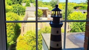 A model lighthouse on a windowsill with a view of a green landscape and buildings. - Charming cottage with character features (Cornwall)