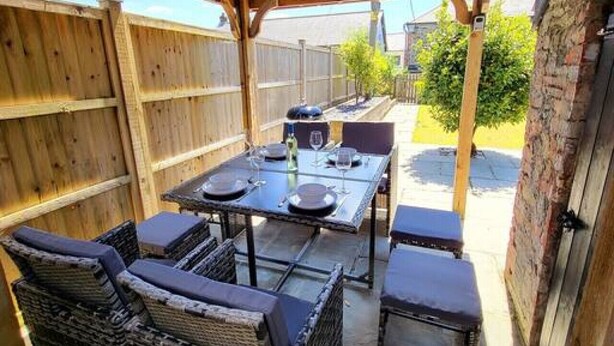 A covered patio with a wooden ceiling, a table set for dining, and wicker furniture. - Charming cottage with character features (Cornwall)