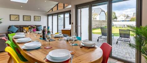A dining area with a large wooden table set for a meal, surrounded by colorful chairs.