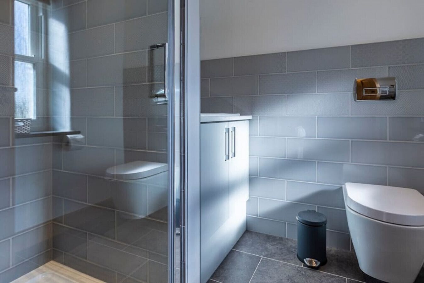 A modern bathroom with a glass shower enclosure, a toilet, and a cabinet.