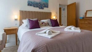 A neatly made bed with a quilted bedspread, pillows, and rolled towels on a wooden headboard. - Modern, luxury bungalow - perfect for families or friends to relax! (Cornwall)
